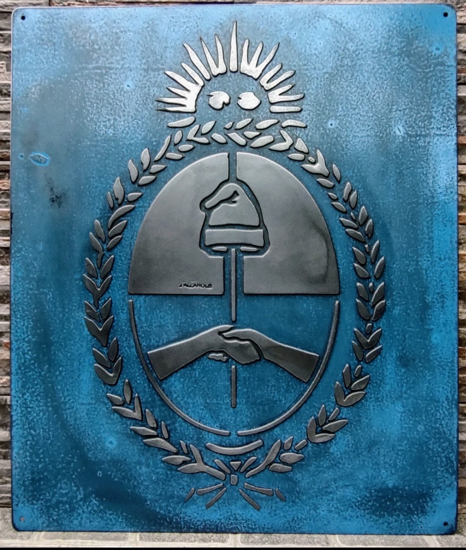 Vista frontal completa del escudo argentino sobre una placa azul de hierro vintage