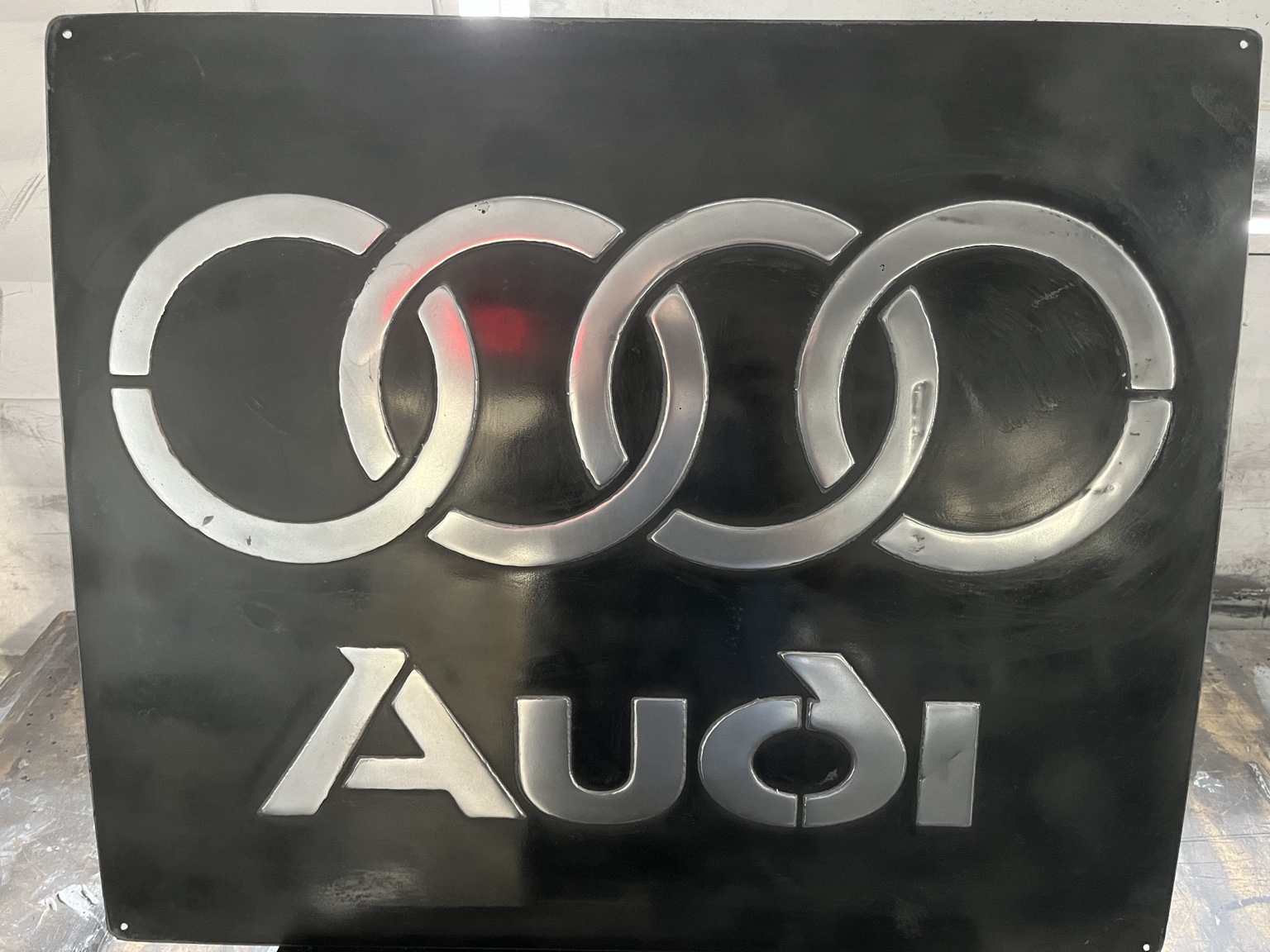 Vista frontal completa de un letrero Audi de hierro negro con aros y letras plateados en relieve