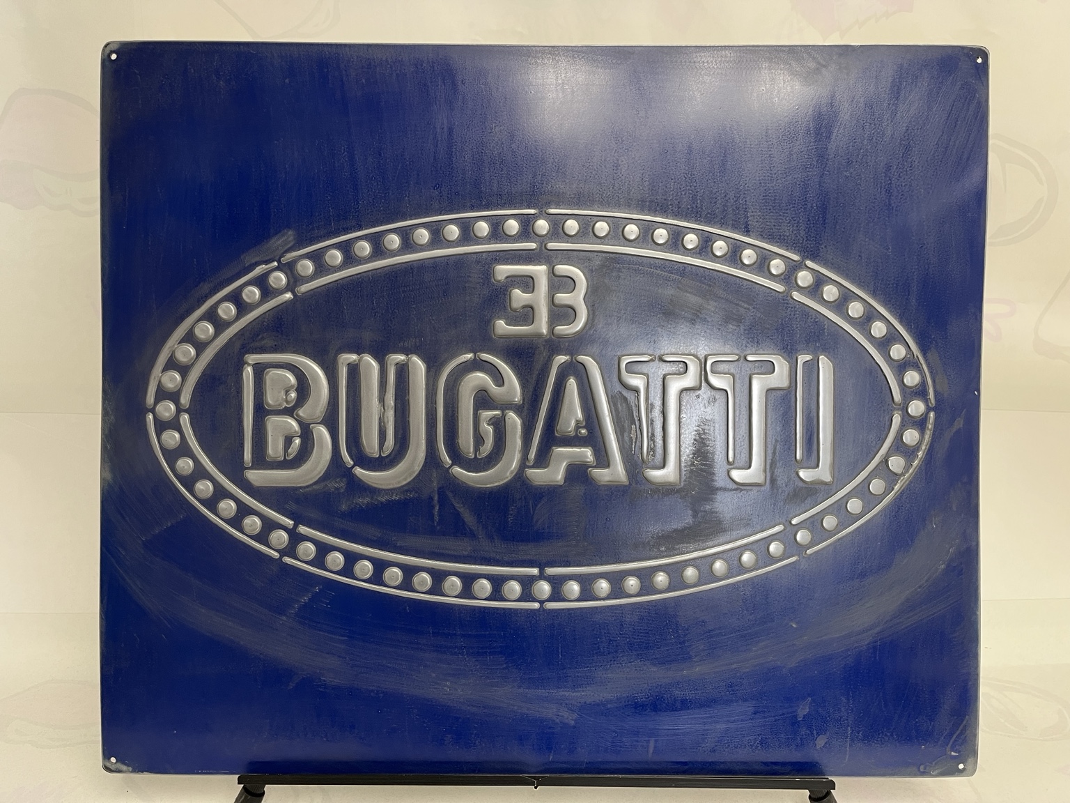 Vista frontal completa de un letrero Bugatti azul de hierro con letras plateadas y número 33 en relieve