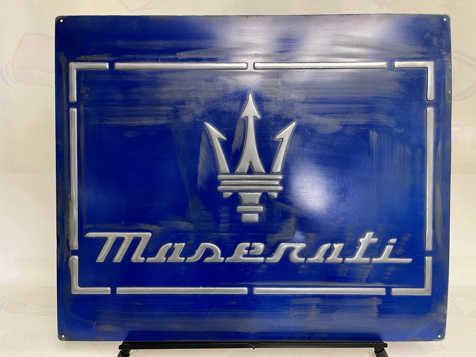 Vista frontal completa de un letrero Maserati azul de hierro con tridente y letras plateados en relieve